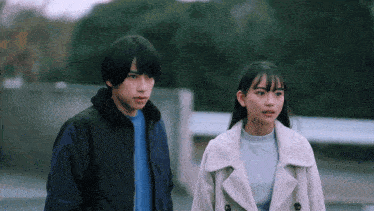 a boy and a girl standing next to each other looking at something