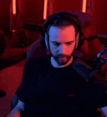 a man with a beard wearing headphones is sitting in front of a microphone in a dark room .