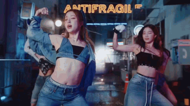 a group of young women are dancing in front of a neon sign that says antifragile