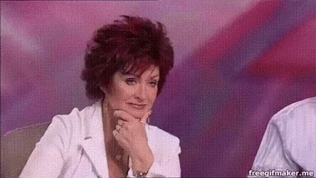 a woman with red hair is sitting in a chair with her hand on her chin and looking at the camera .