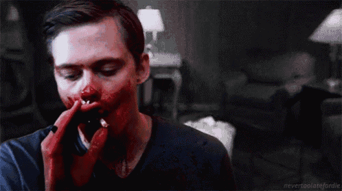 a man with blood on his face is talking on a cell phone in a living room .