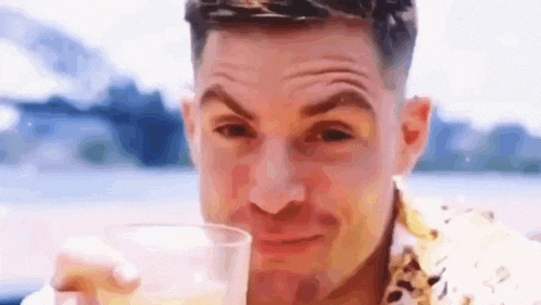 a man is drinking a glass of beer and making a face .
