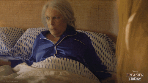 an older woman is laying in bed with a disney freakier friday ad behind her