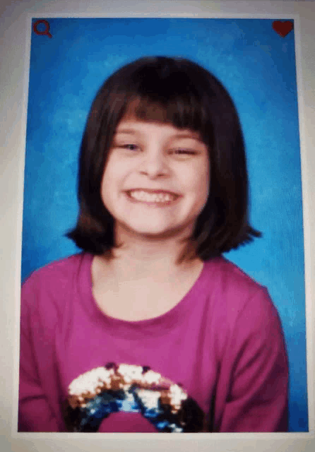 a little girl in a purple shirt is smiling for the camera