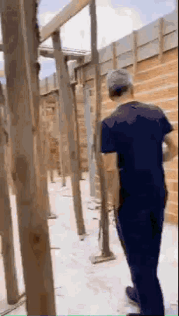 a man in a purple shirt is standing in front of a wooden wall .