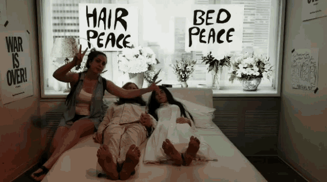 two women sitting on a bed holding a sign that says hair peace