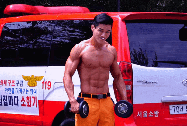 a shirtless man holds a dumbbell in front of a red and white van with the number 119 on the side