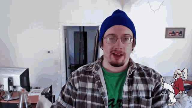 a man wearing a plaid shirt and a blue beanie stands in front of a sign that says ' karate '