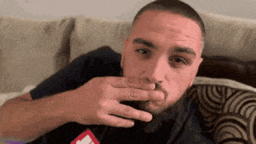 a man with a beard is sitting on a couch and covering his mouth with his hand