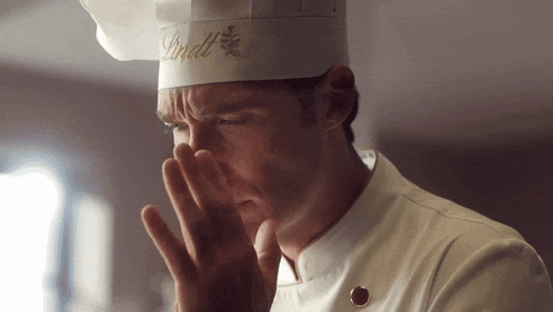 a chef wearing a lindt hat covers his nose with his hand