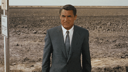a man in a suit and tie is standing in front of a bus stop sign