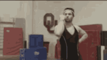 a man wearing a headband and a black tank top is standing in a gym in front of a sign that says q.