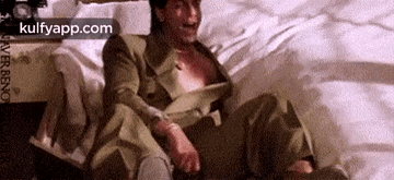 a man in a suit is sitting on a bed with his shirt open .