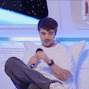 a man is sitting on a couch holding a microphone and looking at his phone .
