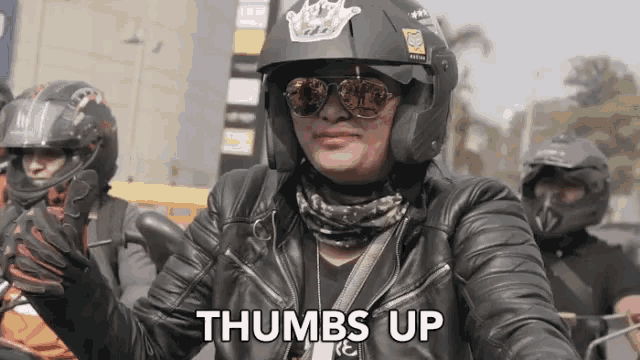 a woman wearing a helmet and sunglasses is giving a thumbs up
