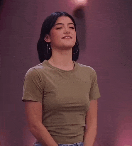 a woman wearing a green t-shirt and jeans is smiling and making a funny face .