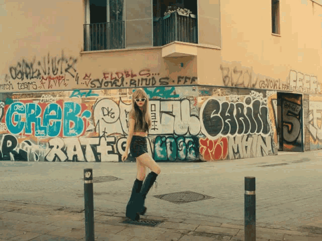 a woman stands in front of a wall that has graffiti on it including the letters chris