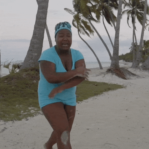 a woman in a blue shirt and shorts stands on a beach