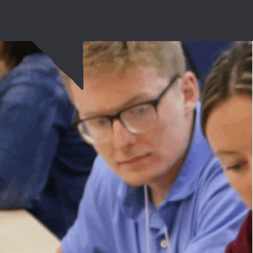 a man wearing glasses and a blue shirt sits at a desk