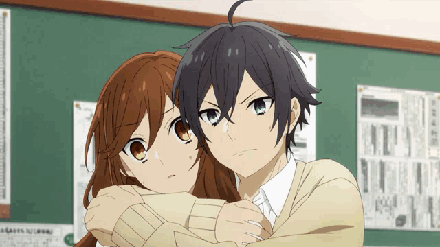 a boy and a girl are hugging each other in front of a green board