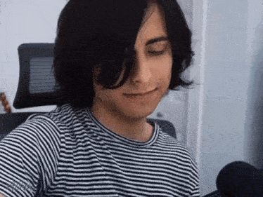 a young man with long black hair is wearing a striped shirt .