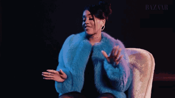 a woman in a blue fur coat is sitting in a chair with her arms outstretched .