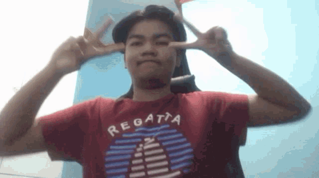 a young man wearing a red regatta t-shirt is making a peace sign