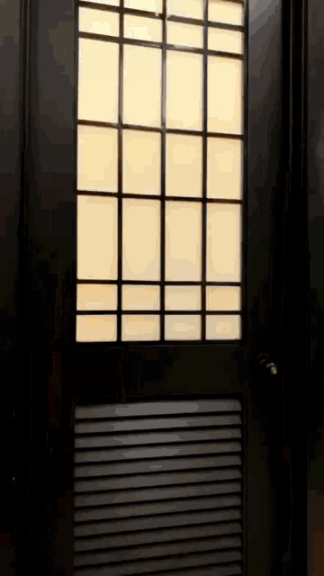 a black door with a grid of squares and a light behind it