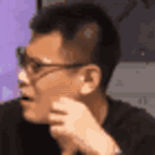 a man wearing glasses is sitting at a table with his hand to his face .