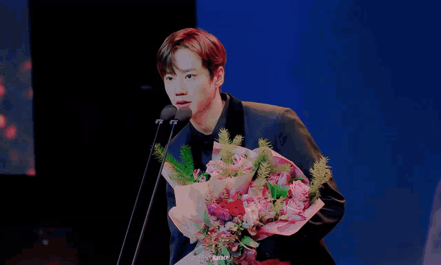 a man in a suit is holding a bouquet of flowers and speaking into a microphone
