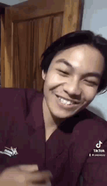 a young man is smiling and making a funny face while sitting in front of a wooden door .