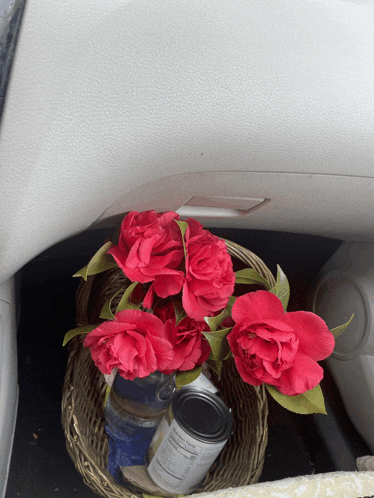 a basket of red roses sits in the trunk of a car next to a can of food