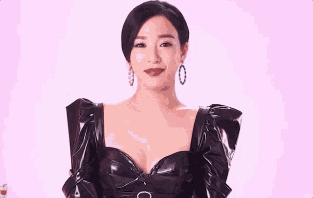 a woman wearing a black leather dress and earrings is smiling .