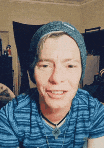 a man wearing a blue striped shirt and a grey beanie with the word petra on it