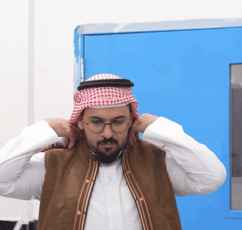 a man wearing glasses and a scarf around his head stands in front of a blue door