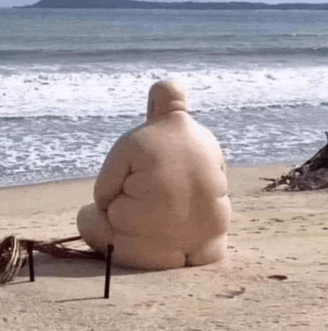 a statue of a fat man is sitting on the beach looking at the ocean .