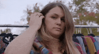 a woman is standing in front of a rack of clothes holding her hair .