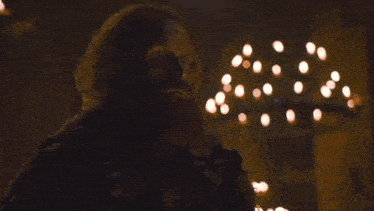 a man with a beard is standing in front of a chandelier with candles