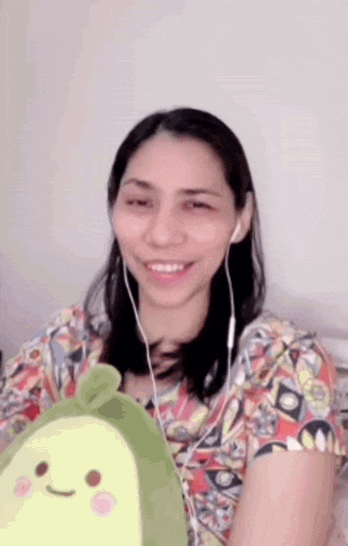 a woman wearing headphones and holding an avocado stuffed animal .