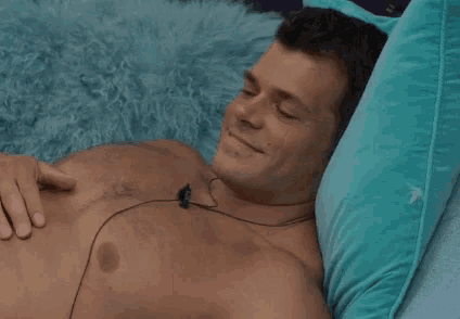 a shirtless man is laying on a bed with a pillow and headphones on his chest .