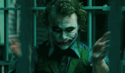 the joker is holding a knife in his hand in a dark room .
