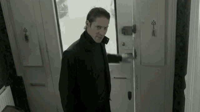 a man in a black jacket is standing in front of a door