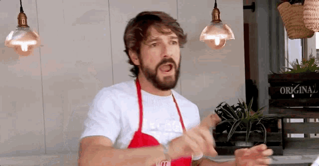 a man with a beard wearing a red apron and a white shirt is making a funny face .