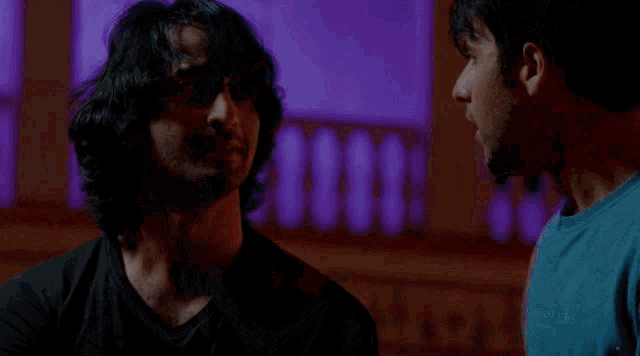 two men are standing next to each other in a dark room . one of the men has his arm around the other 's shoulder .