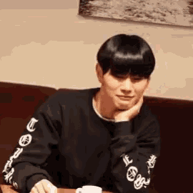 a young man is sitting at a table with his hand on his chin and a cup of coffee .