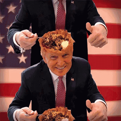 a man in a suit and tie is holding a pie in front of his head and giving a thumbs up