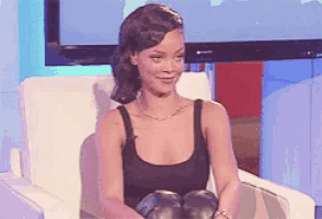 a woman in a black tank top sits in a chair with her hands on her knees