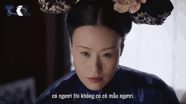 a woman in a blue dress with a flower in her hair looks at the camera with the words có người thì không có có mẫu người