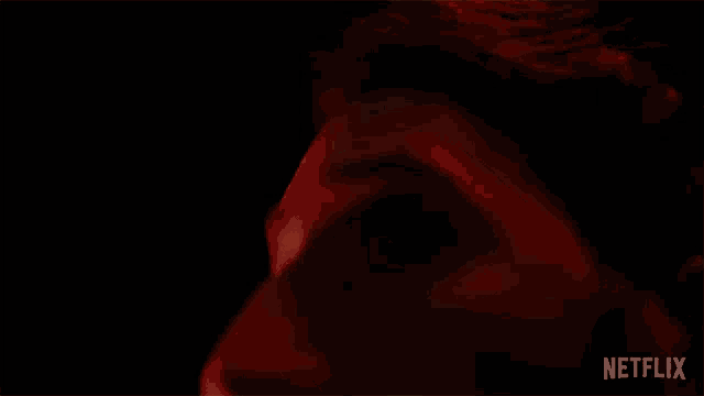a close up of a person 's eye in a dark room with a red light behind it .