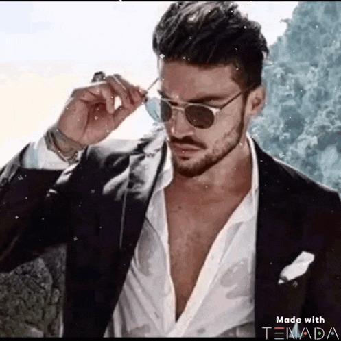 a man in a suit and sunglasses is adjusting his glasses .
